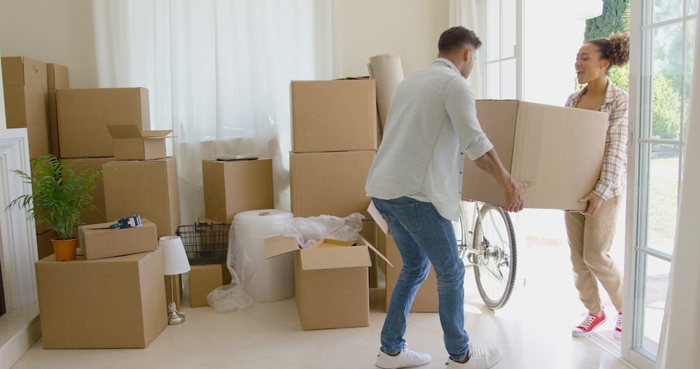 Moving Day Tips | Couple moving boxes into new apartment and stacking them in the corner