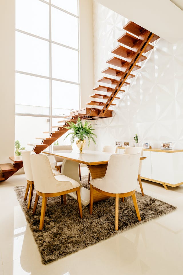 Gorgeous clean light filled dining room with a dining table and side bar and a floating stair case.